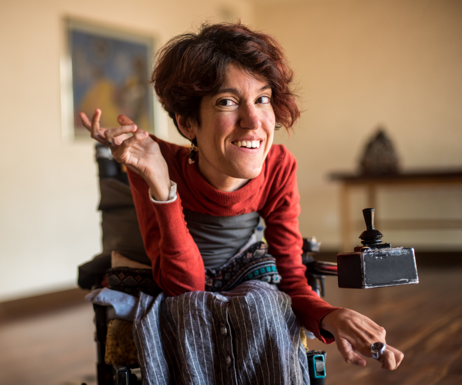 A smiling woman who uses a motorized wheelchair gestures as she talks with another person.