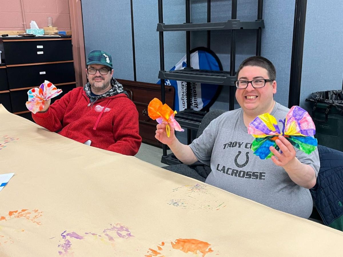 Craft class participants hold up the paper butterflies they made.
