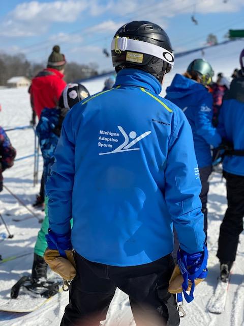 Person wearing Michigan Adaptive Sports jacket at adaptive skiing event.