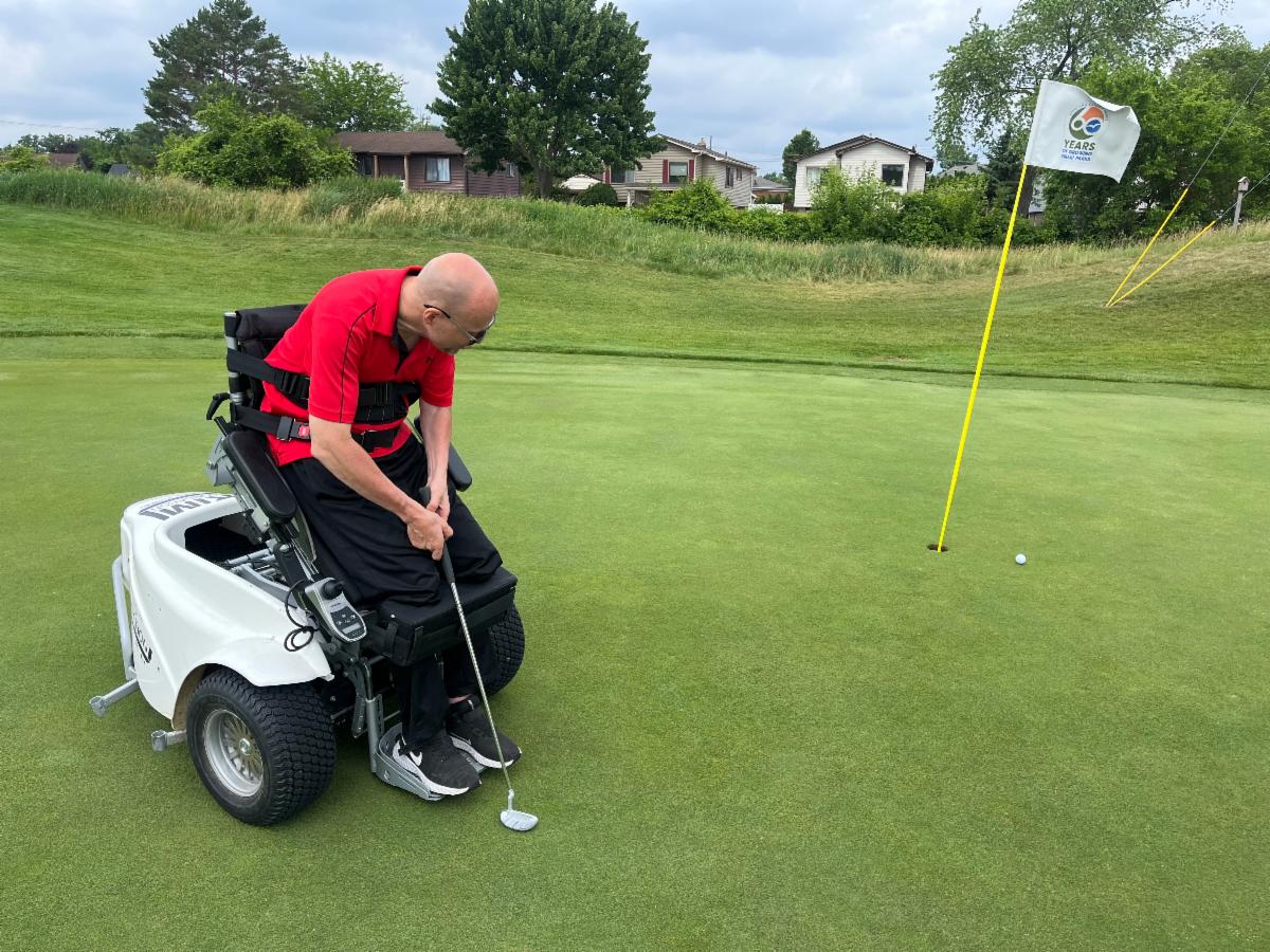 A man is using an adaptive golf cart to support him while standing to putt.