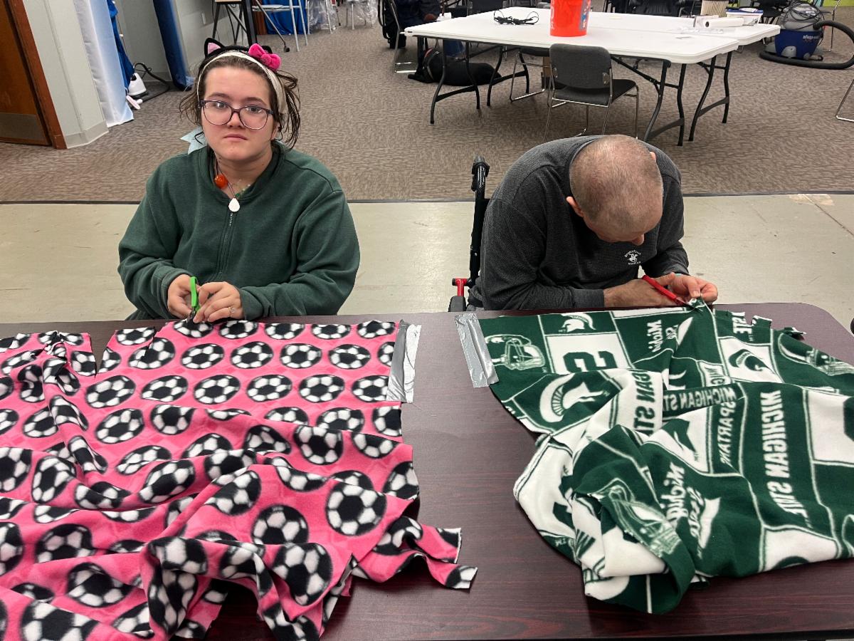 People are cutting fringe on fleece blankets that they are making in a class.