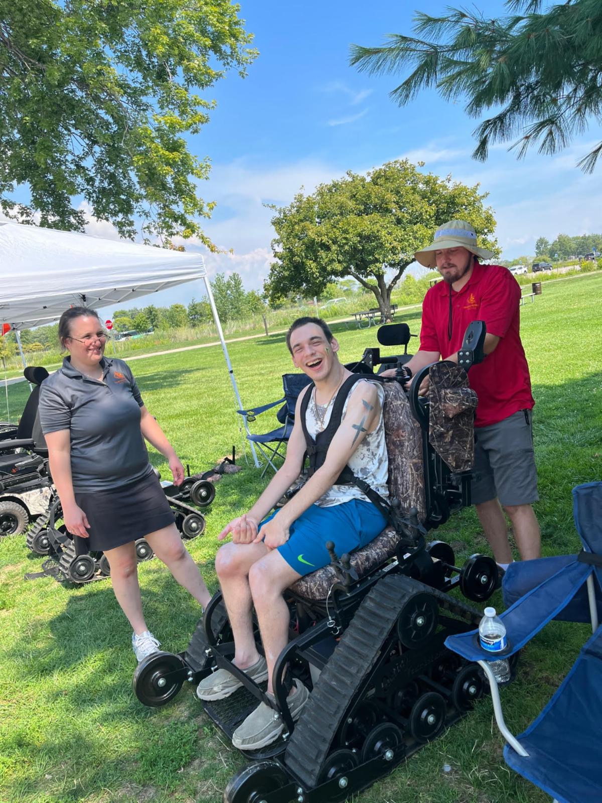 A young man prepares to use a track chair with the help of two volunteers.