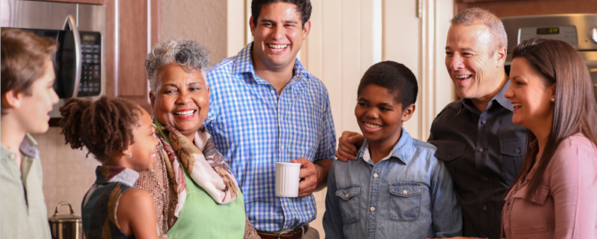 A multigenerational family standing together in a kitchen, smiling and enjoying each otherâs company. 