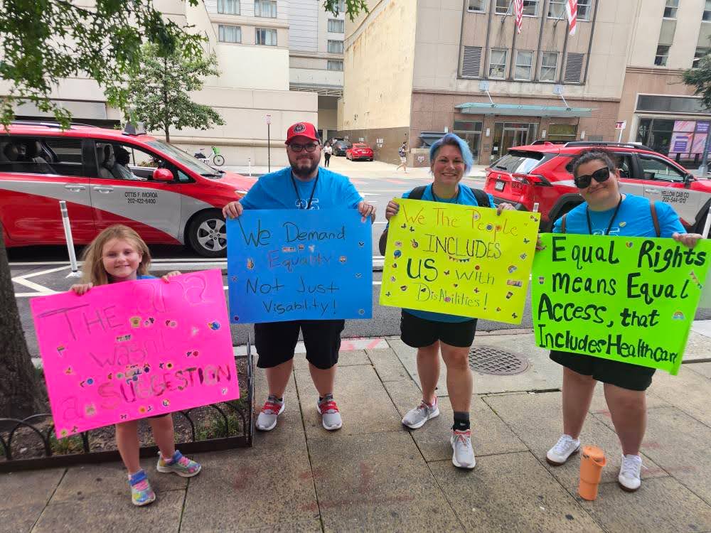 Disability Network Eastern Michigan staff and family hold signs protesting the One Big Beautiful Bill Act in Washington DC in July 2025.
