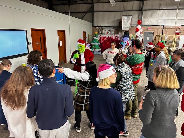 A diverse group of people listen and dance to the Grinch singing karaoke.