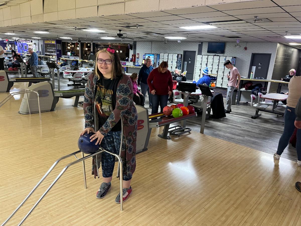 A young woman smiles as she sets a bowling ball on a bowling ramp in a bowling alley.