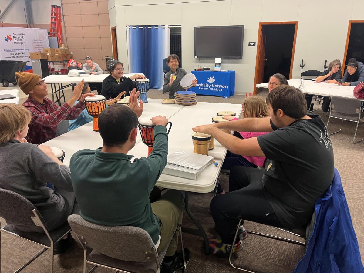 9 people are gathered around a table playing percussion instruments.