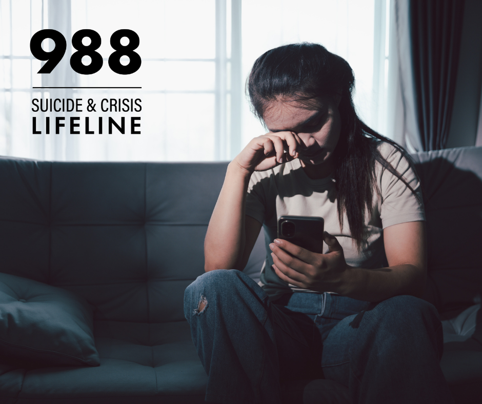 A young woman overwhelmed by emotion is sitting alone on a couch, looking at her phone.