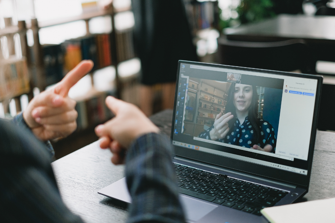 A woman is learning American Sign Language on a video chat on a laptop.