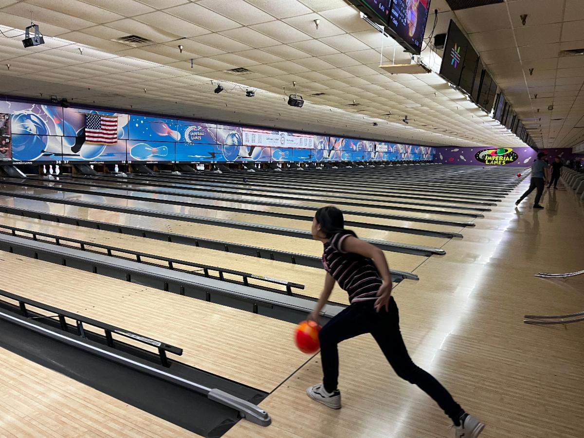A young woman swings a bowling ball, preparing to throw it down a lane with bumper guards.