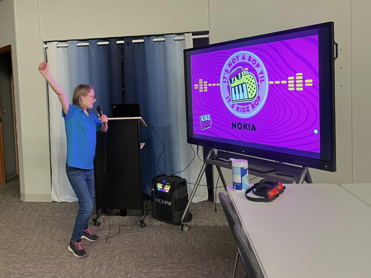 A person sings karaoke enthusiastically as they read lyrics from a large screen.