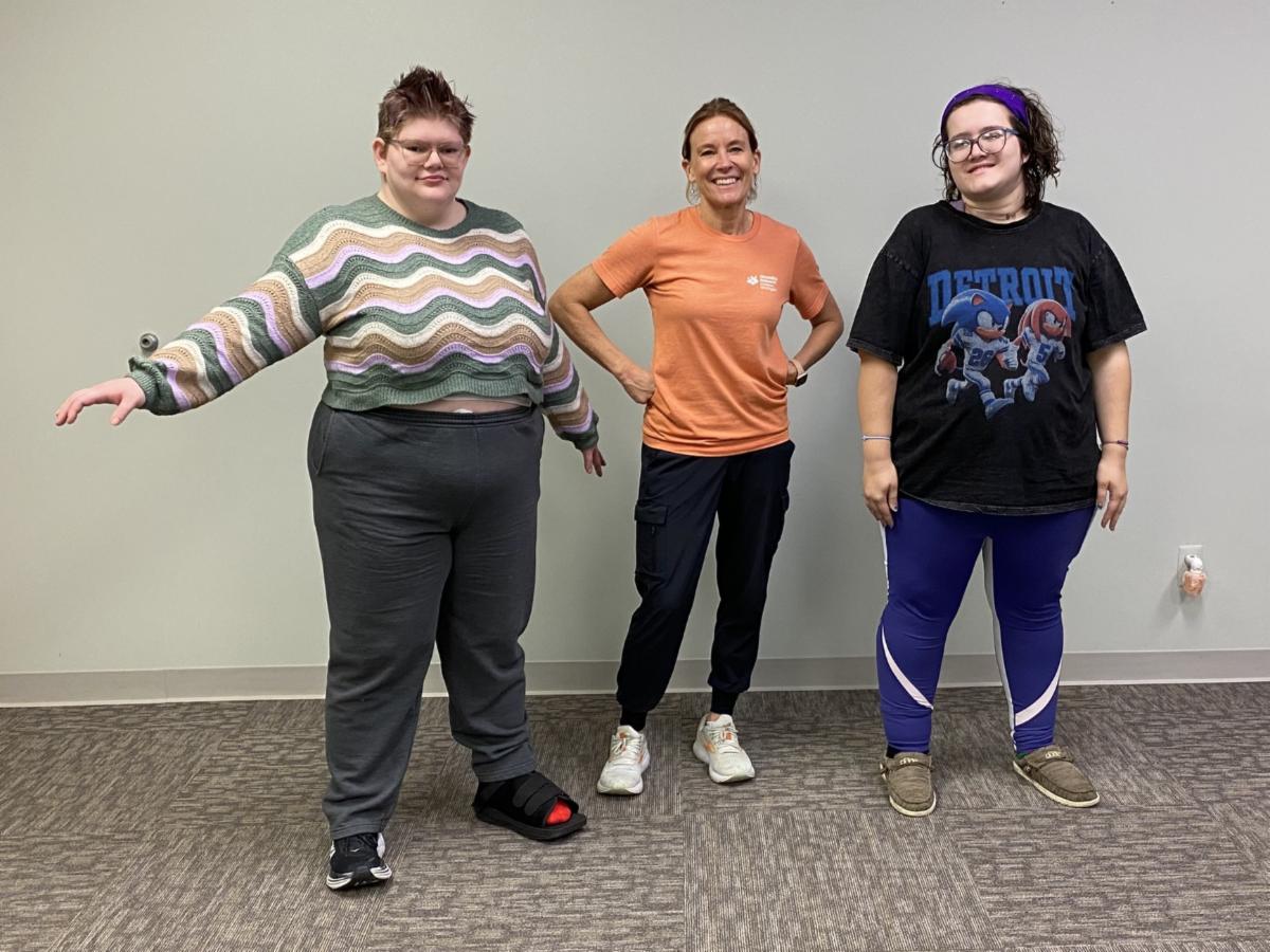 A female instructor poses with two young woman in a dance class.