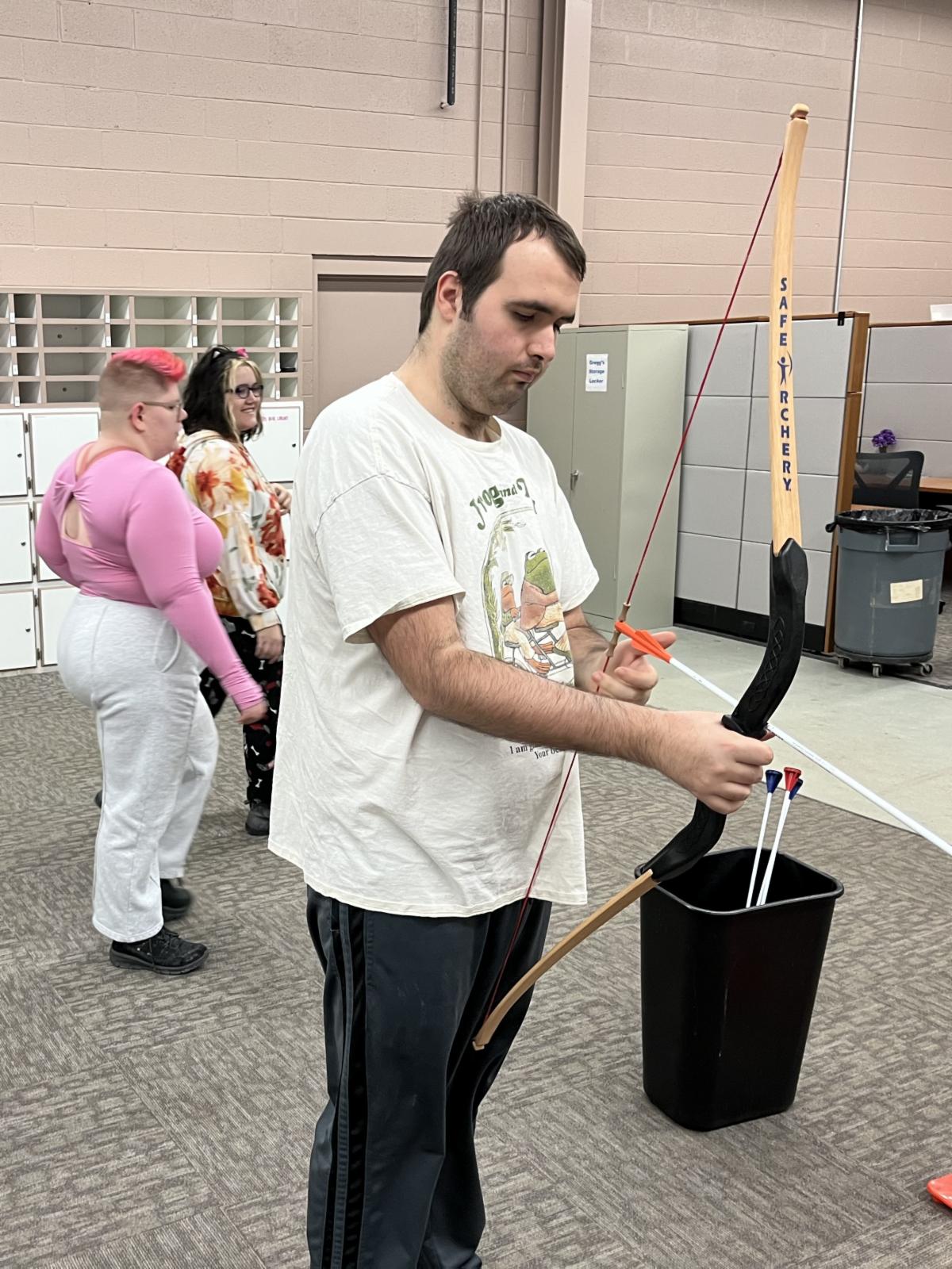 A man is putting an arrow in a quiver for stick'em archery. Other adaptive recreation participants are in the background.