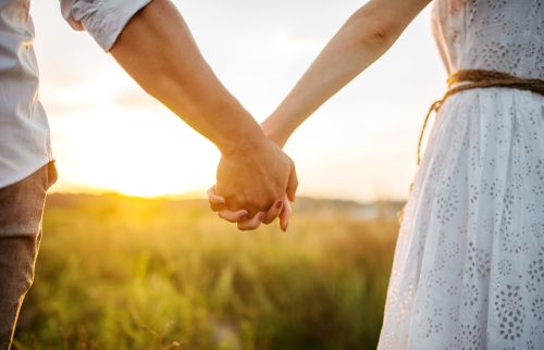 Couple hold hands in green field on sunset