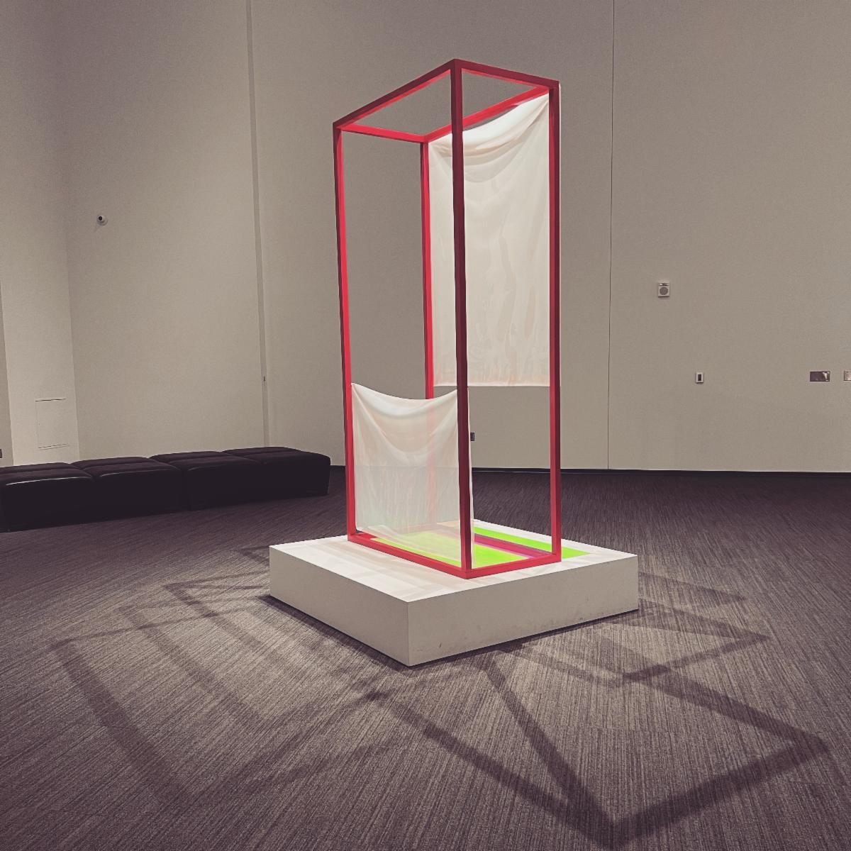 Frame sculpture with textile pieces, shadows show multiple boxes in patterns reflecting off it. 