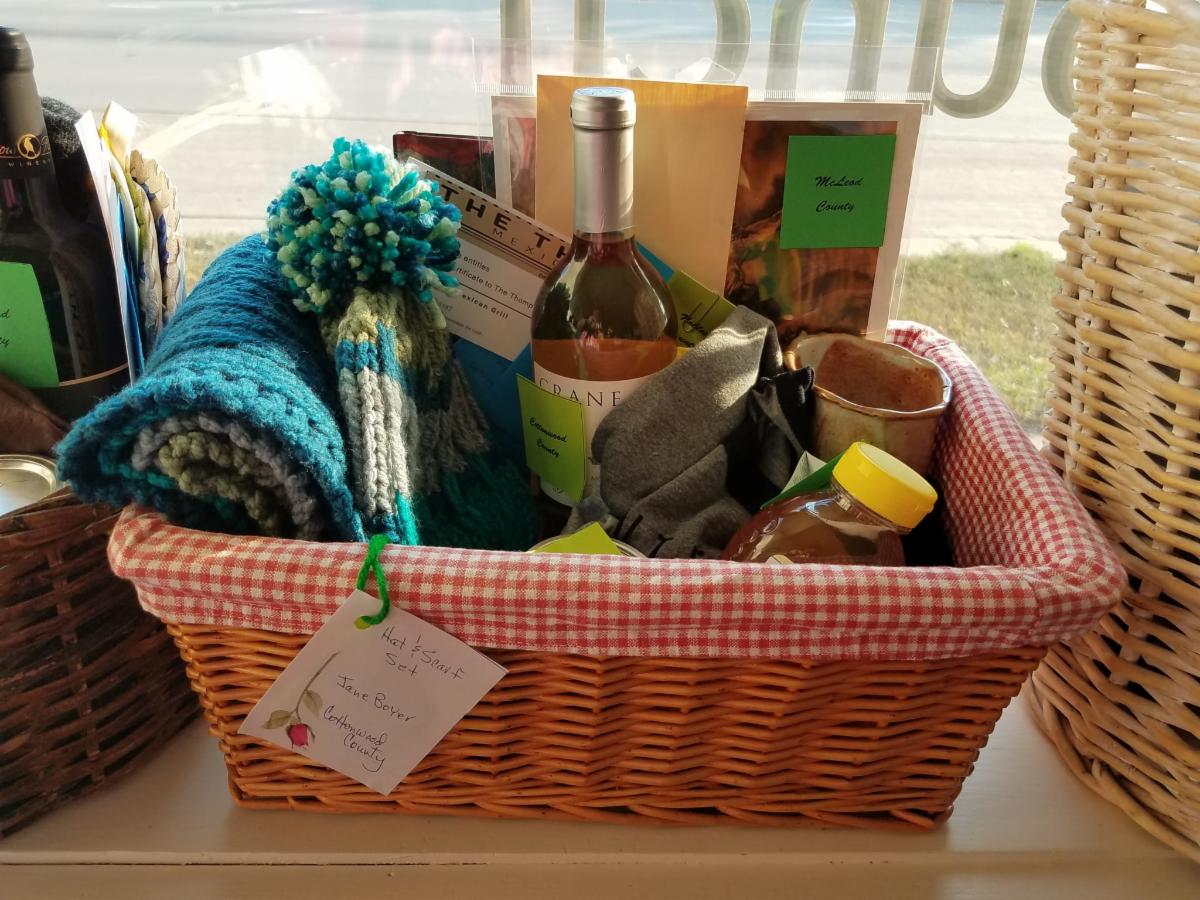 Basket of goods like honey, hat, scarf, wine, pottery mugs and more