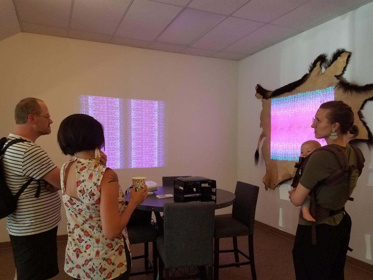 Three people view projected artwork on 2 walls.