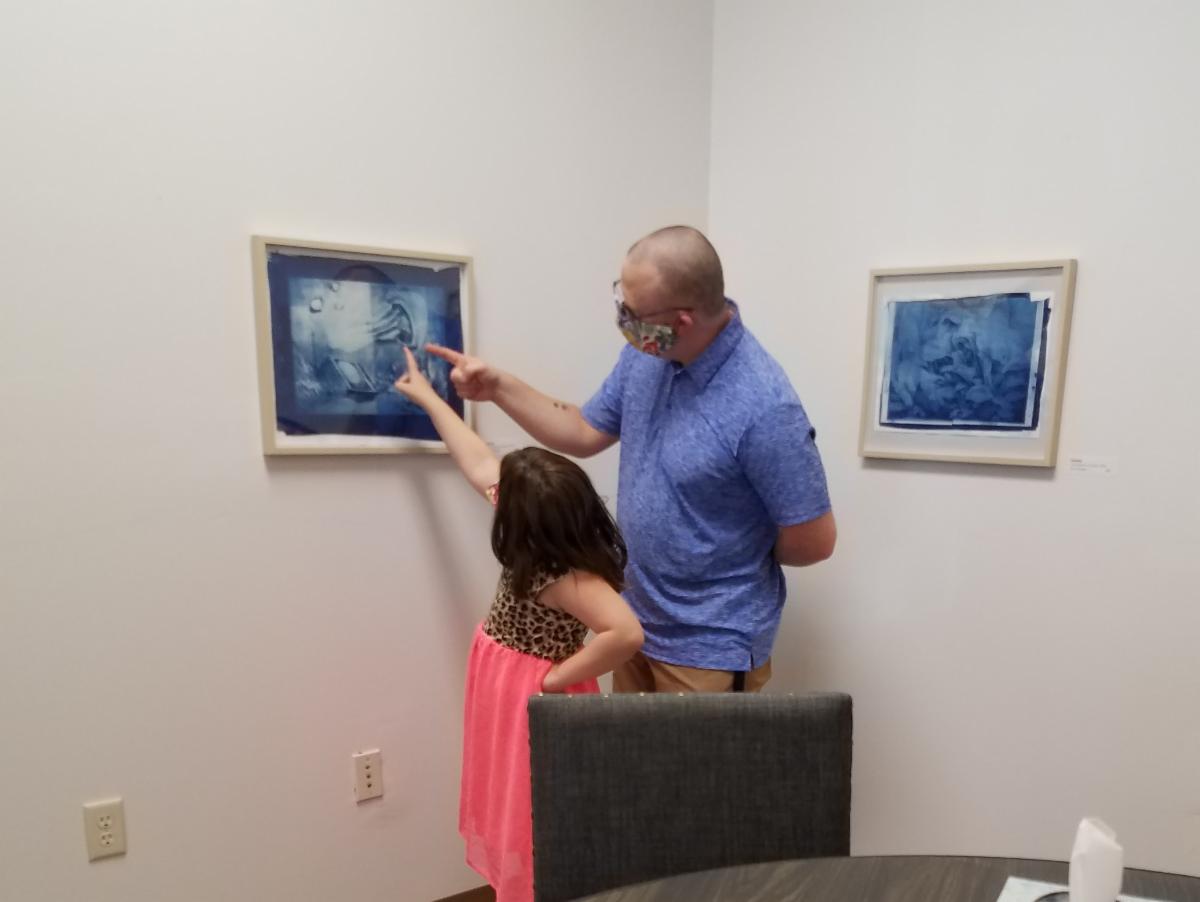 A father and his child look at Anne's artworks at the gallery.