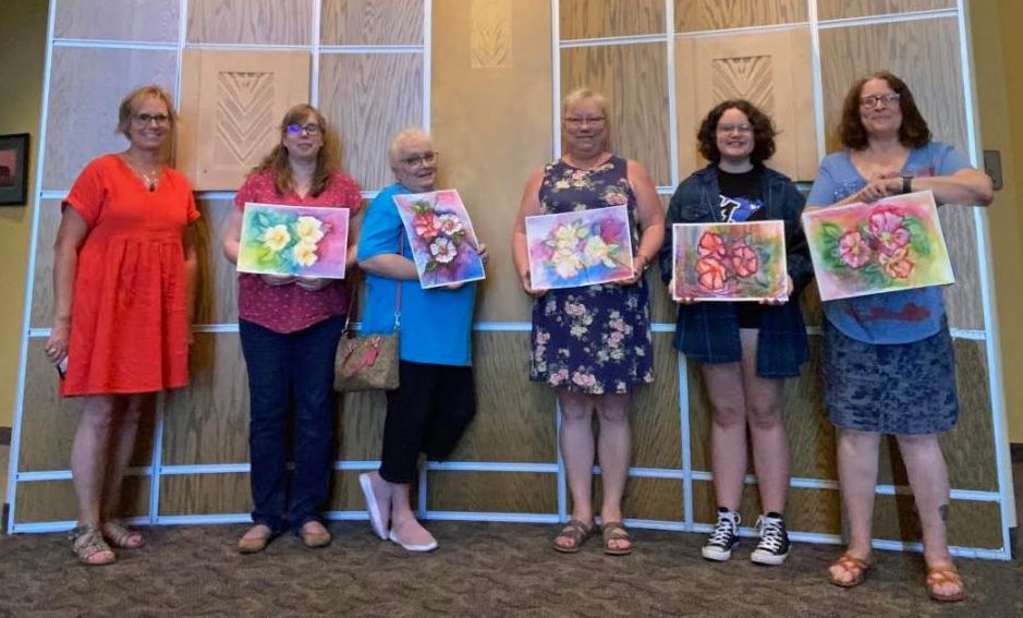 5 students and the instructor, Tamara Isfeld, pose with watercolor flower paintings.