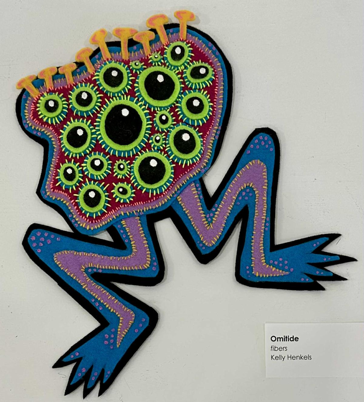Fiber art of a creature with 2 legs and many eyes