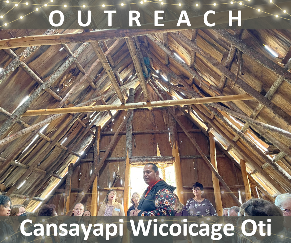 Outreach: Cansayapi Wicoicage Oti (Picture of man inside wood vaulted ceiling building, presenting to people around him)