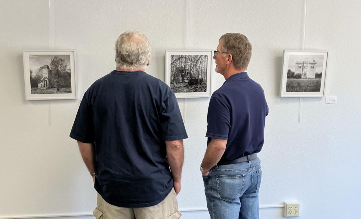 Two figures look at black and white photos on a gallery wall