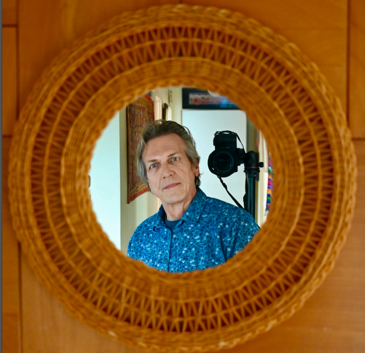 Self portrait photo taken with John looking into a circular mirror, with a camera on a stand behind him. 