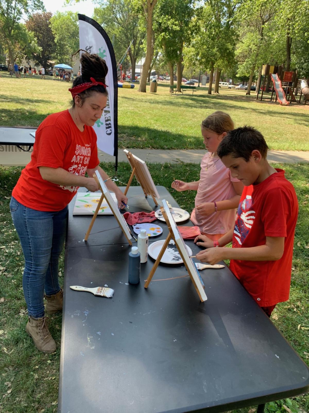 Adult works with two teens painting on canvases outside