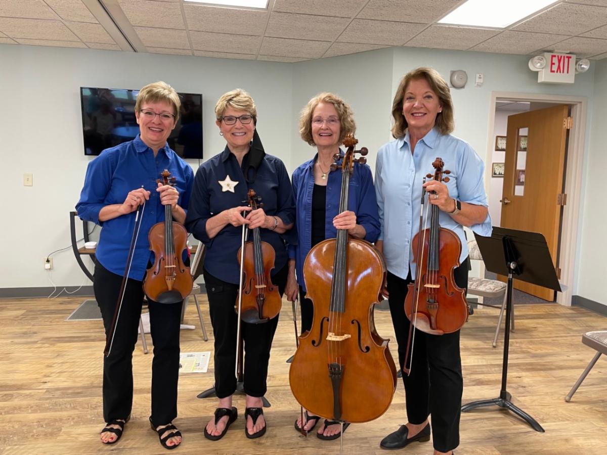 Four women hold their stringed instruments