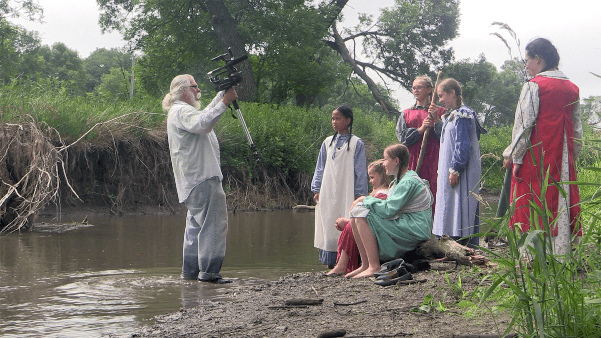 Bill Richards standing in a river with a video camera, talking to a group 