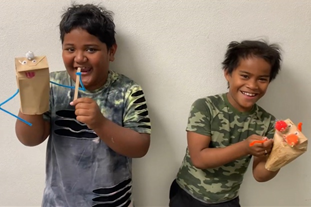 Two kids pose with puppets they've made