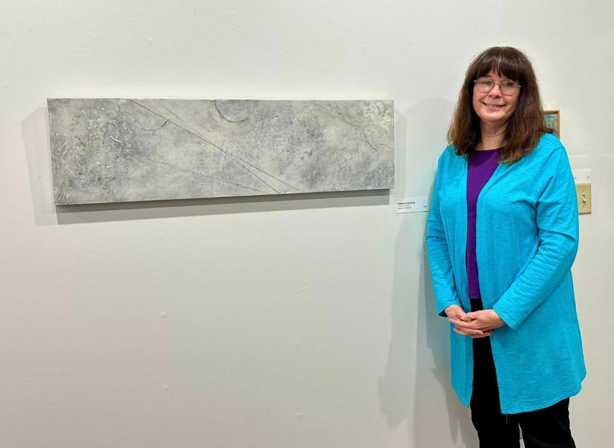 Adrienne stands next to one of her artworks hung in the SMAC gallery