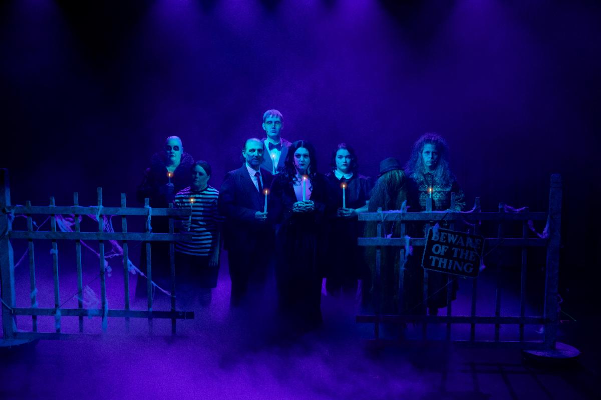 Stage production of The Addams Family musical where the family is in a ark purple lit graveyard holding candles