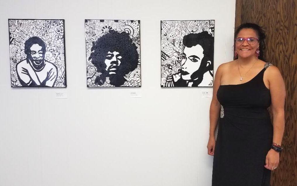 Artist Jammie Niemeyer poses with 3 of her portraits hung in the gallery