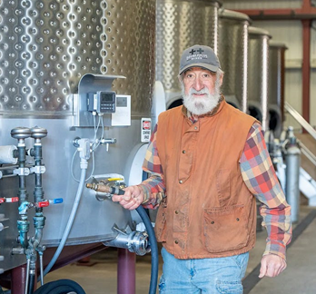 Tom Rinaldi standing beside winemaking equipment inside a winery.