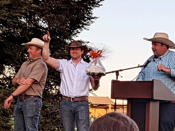 three auctioneers standing on the presentation stage one holding a cake high in the air