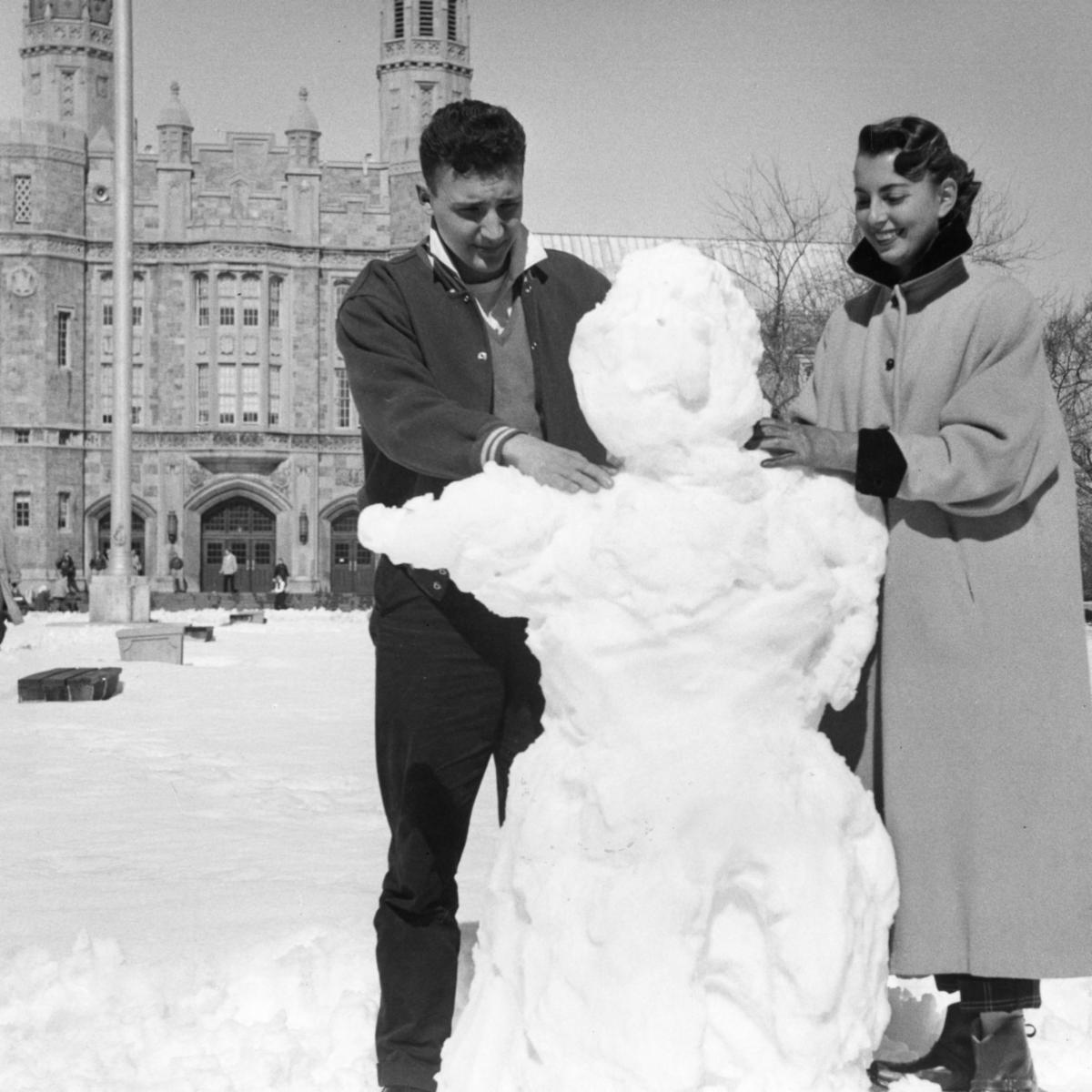 Black and white photo of 2 people and snowman in front of muic building