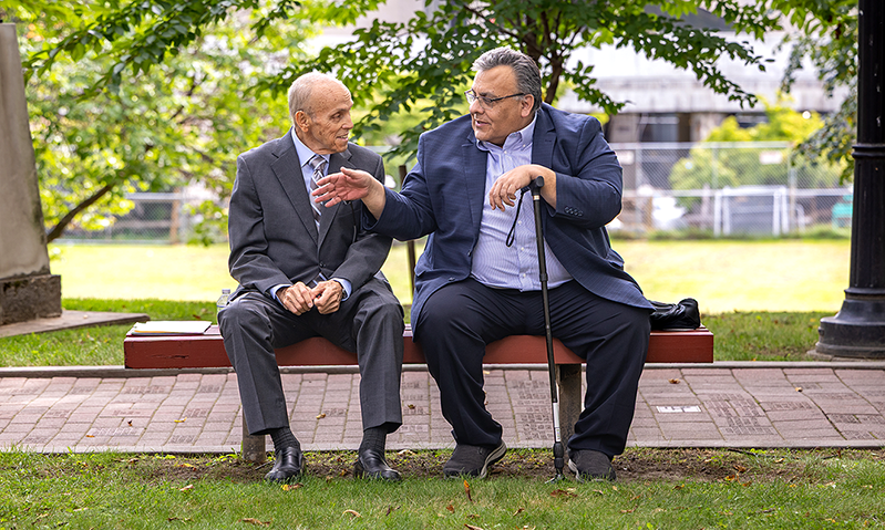 Two Lehman Presidents Chat on a Bench along Alumni Walkway