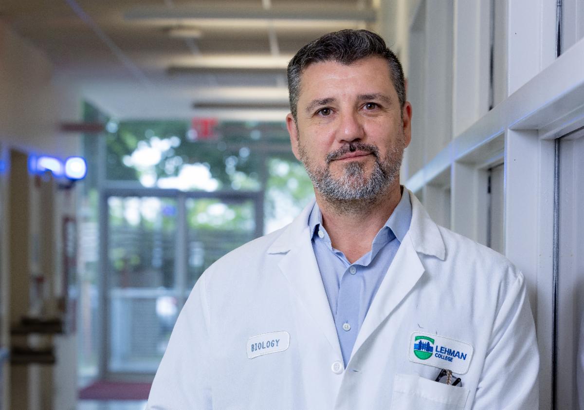 Professor in lab, wearing labcoat with Lehman College logo on it