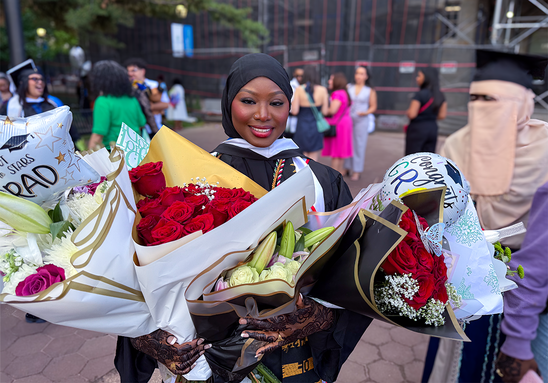 A graduate holds four bouquets of flowers