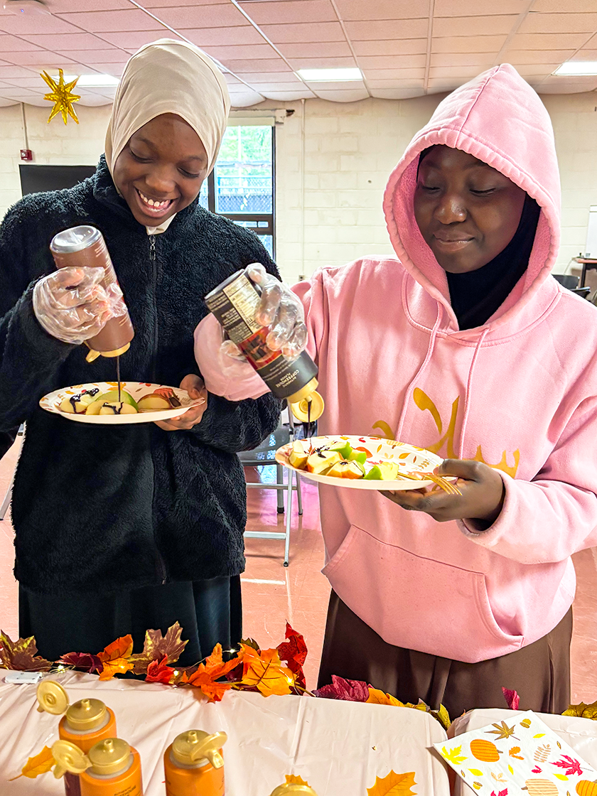 Image of two female students pouring chocolate syrup on apple slices.