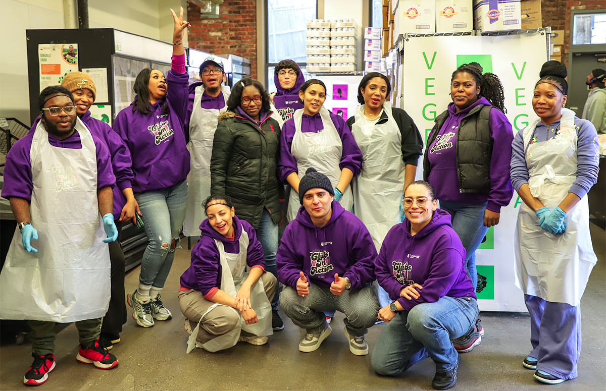 Group posing in aprons and matching purple sweatshirts in kitchen
