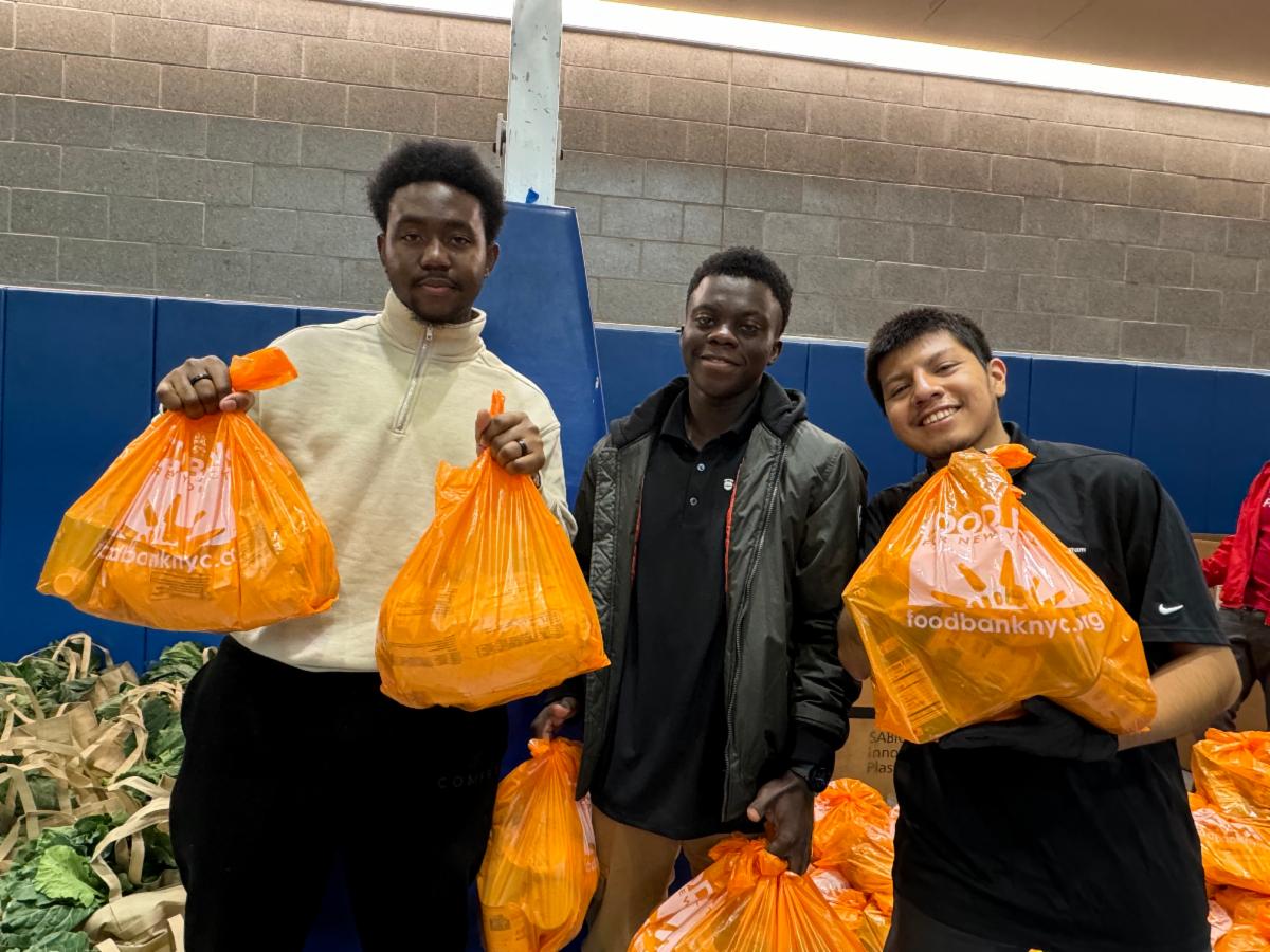 Three students hold up orange food bank bags