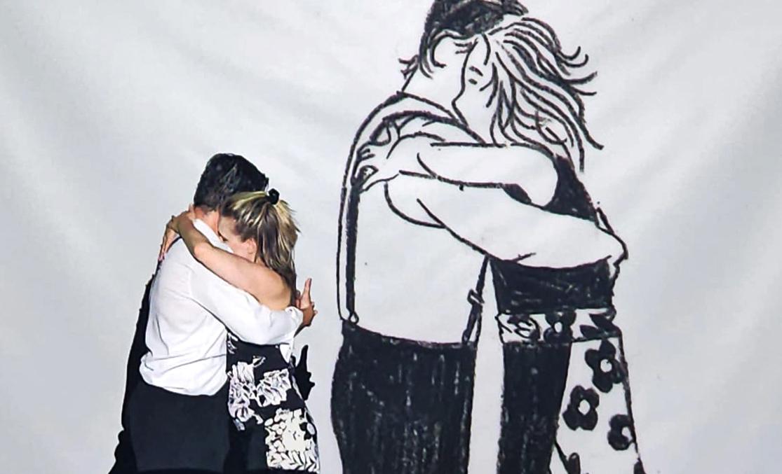Humans hugging in front of a giant illustration of a hug