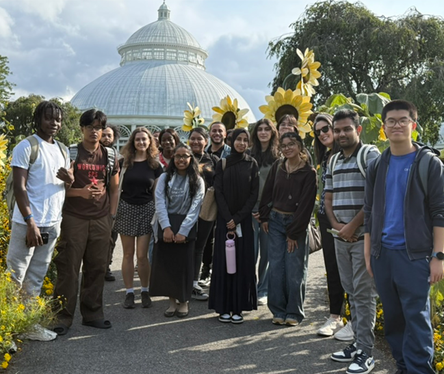 Group of students in front of sunflower art and a greenhouse at NYBG