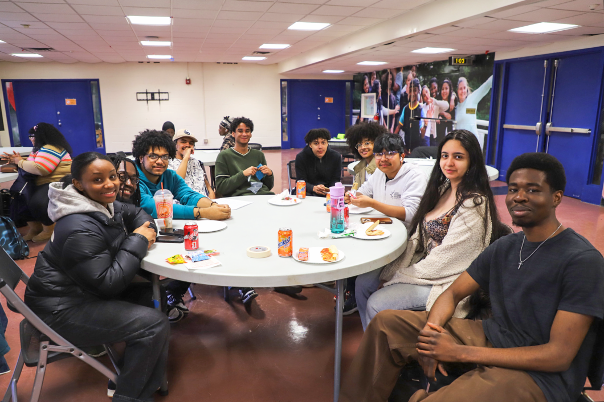 Lehman students smile as they meet new friends seated at a table in student life building