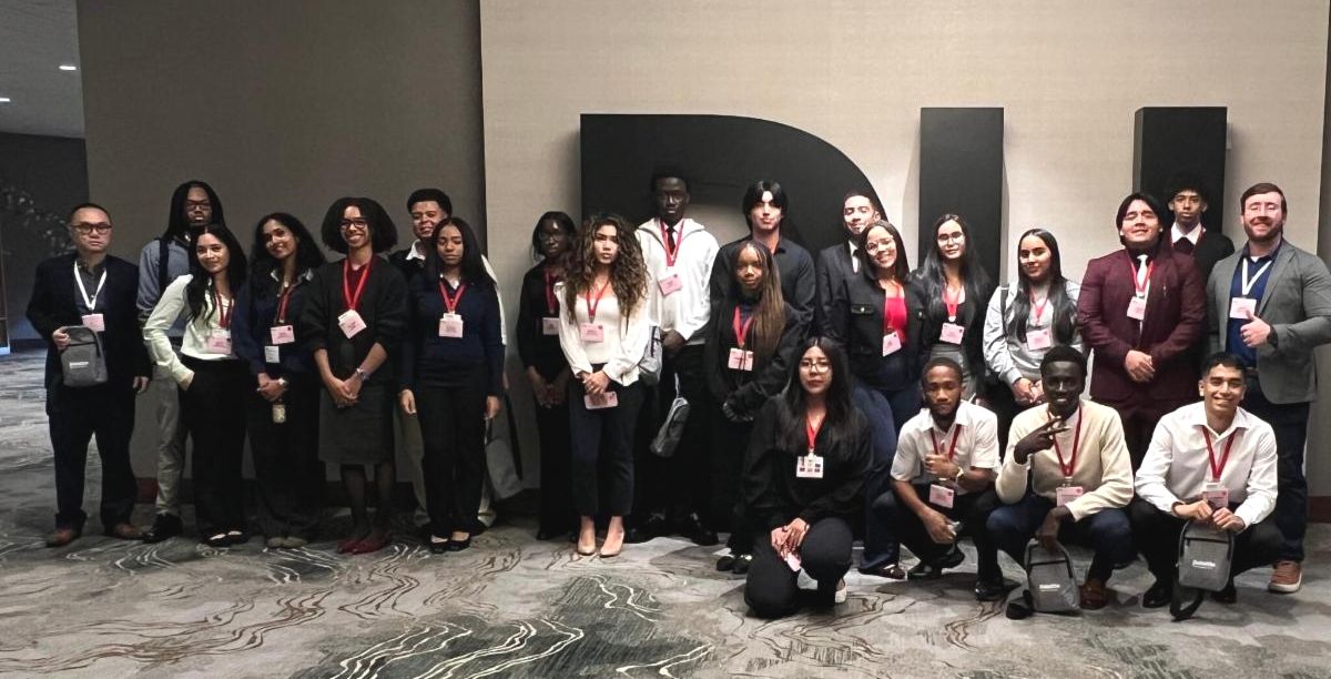 Students posing against a wall with giant typographical DU