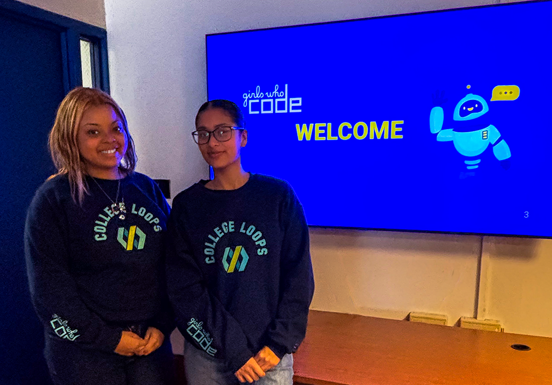 Two students in front of girls who code sign