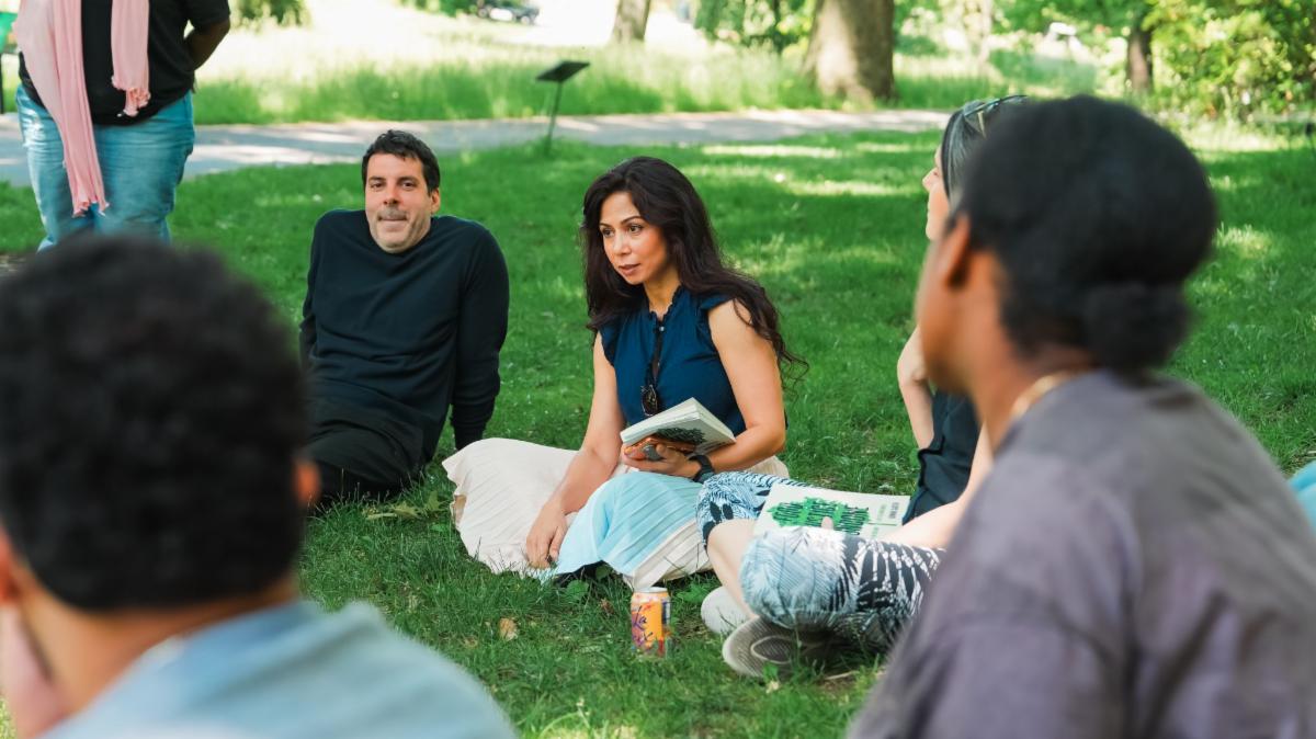 Photo of people sitting on the grass discussing a book.