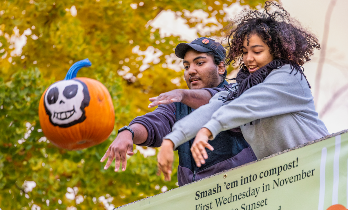 Two people throwing a pumpkin with painted skull face